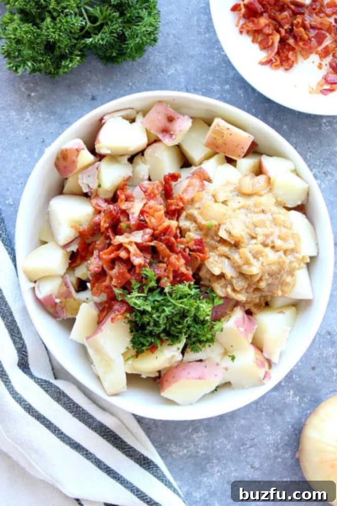 Cooked red potatoes, crispy bacon, and tangy mustard onion dressing in a white bowl, garnished with chopped fresh parsley.