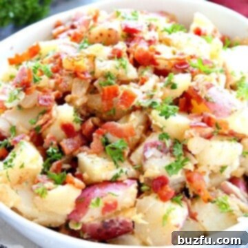 Warm German potato salad in a white bowl with crispy bacon and herbs.