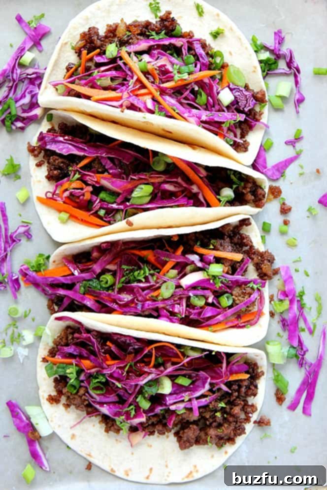 Four Korean Beef Tacos with soft tortillas, filled with seasoned beef and topped with Asian slaw, beautifully arranged on a baking sheet.