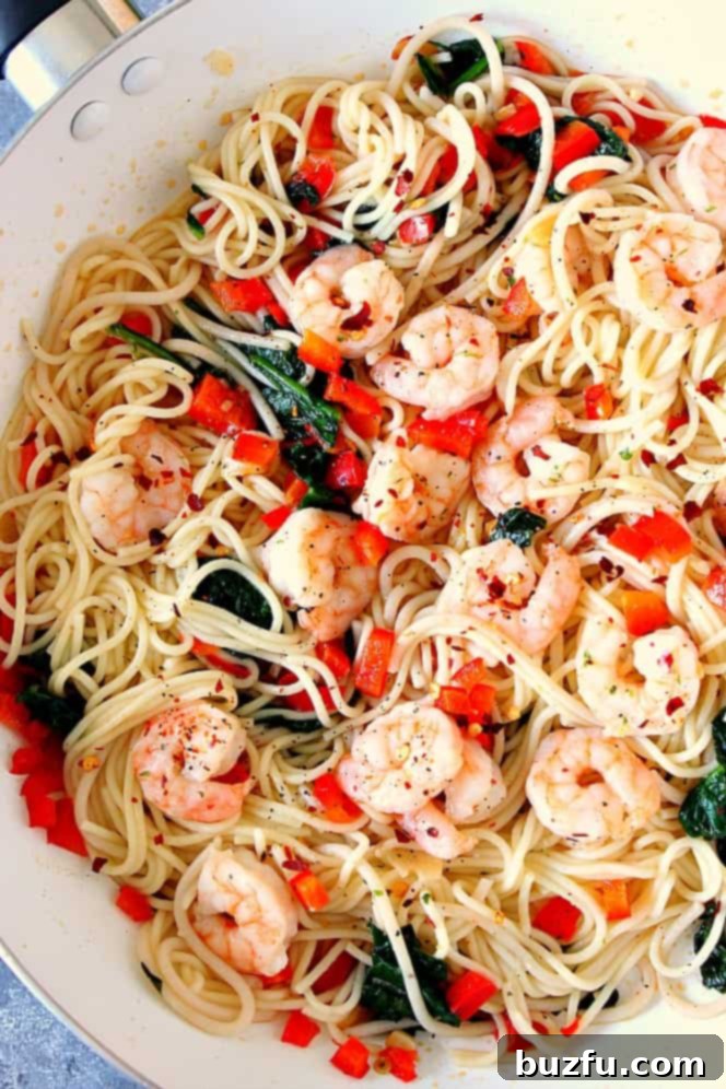 Shrimp Scampi with red peppers and spinach and Angel hair pasta in white cooking pan. 