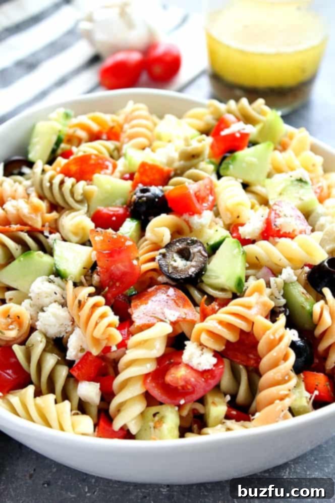 Close up on Italian Pasta Salad in white bowl, with homemade dressing in jar in the background.