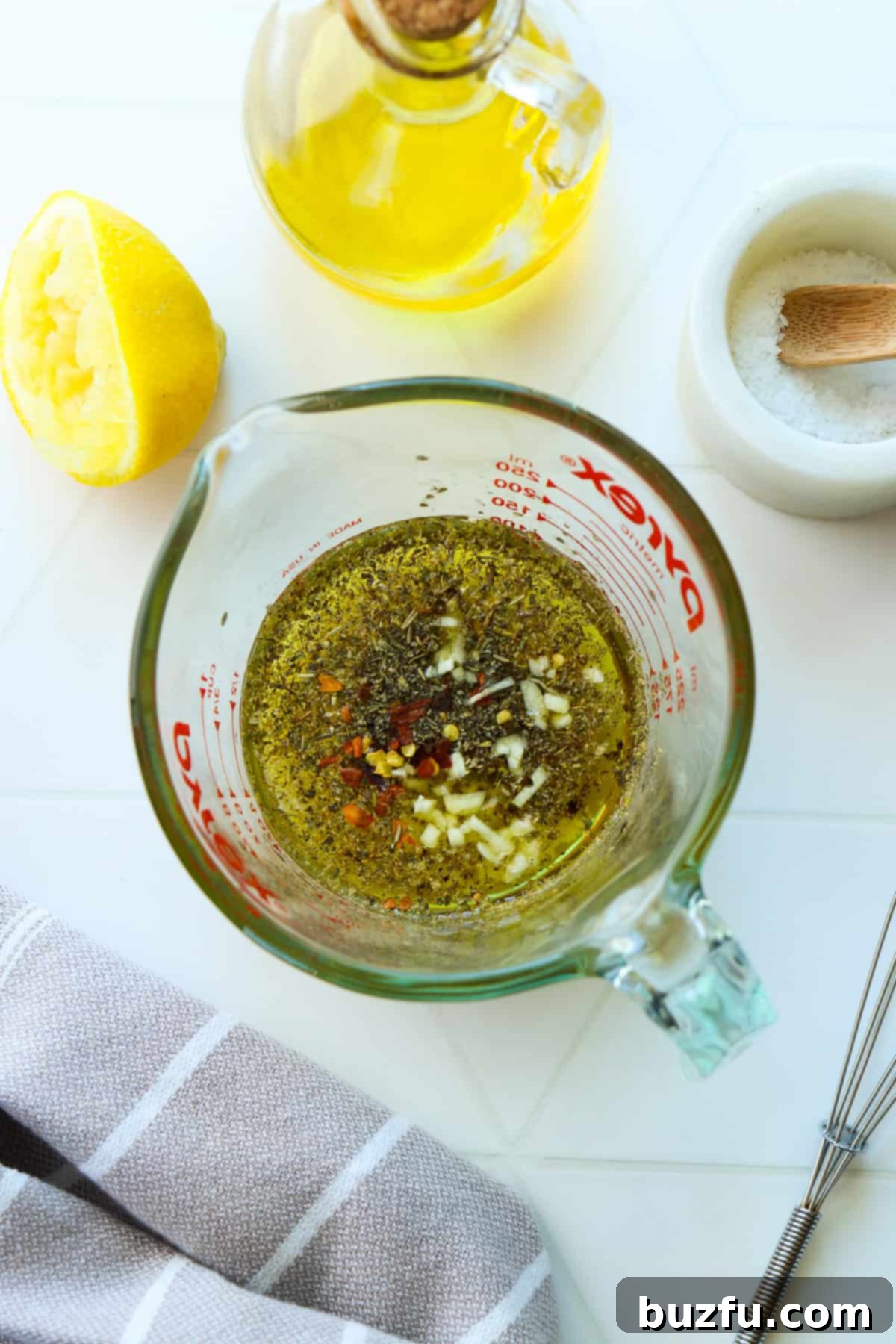 Zesty Italian Dressing 4 All ingredients for Italian dressing being whisked in a clear glass Pyrex cup, with a small silver whisk next to it and a bottle of olive oil behind it.