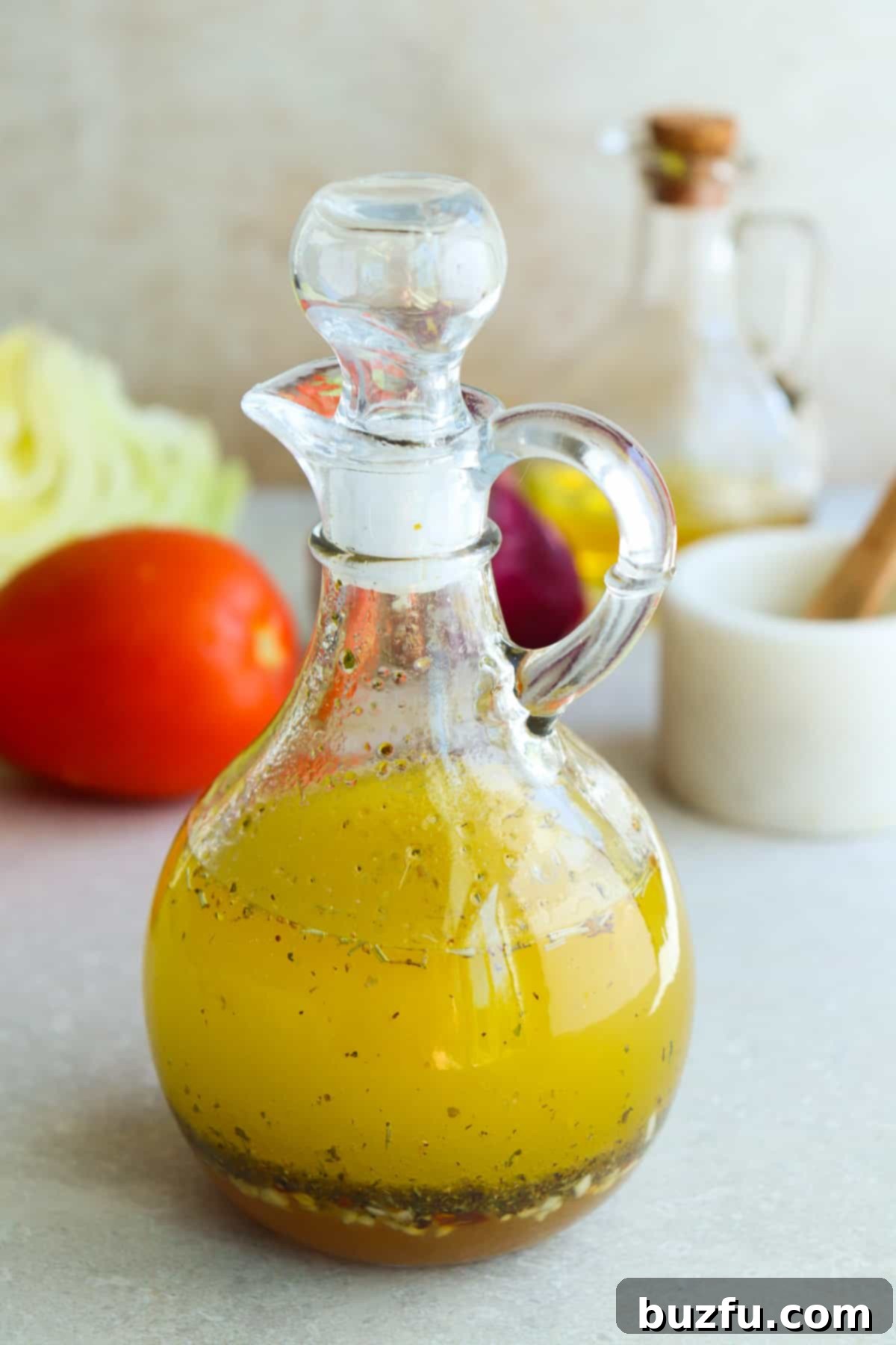 Zesty Italian Dressing 5 Beautifully presented Italian dressing in a glass cruet on a gray wooden board, with fresh, ripe Roma tomatoes in the background, suggesting a perfect salad accompaniment.