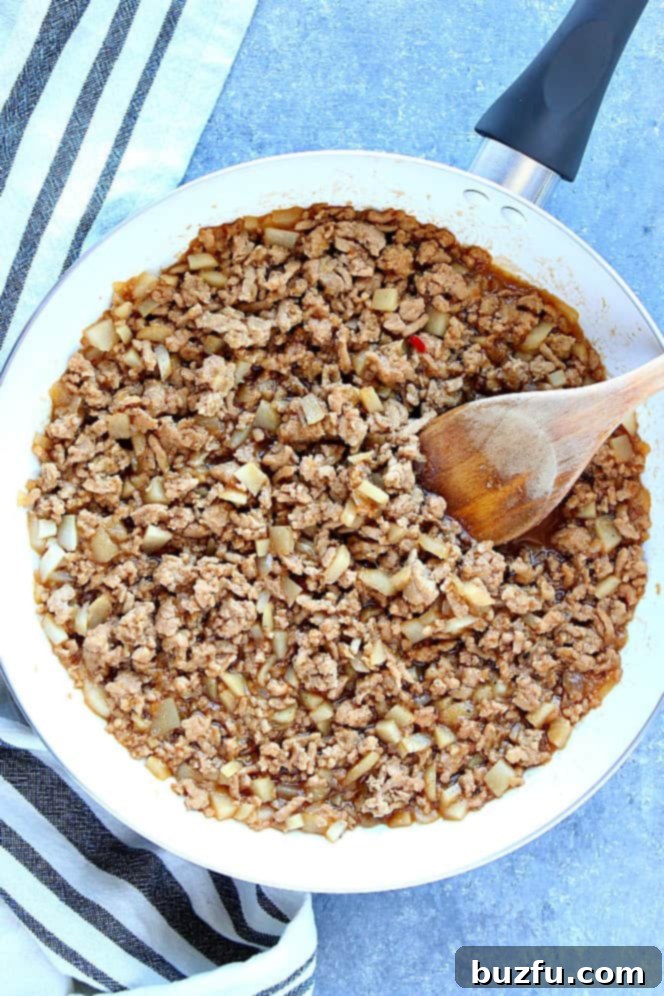 How to make P. F. Chang's Chicken Lettuce Wraps recipe. The savory chicken filling cooks beautifully in a pan. Close-up shot of ground chicken cooking in a white pan, infused with the Asian sauce and aromatics.