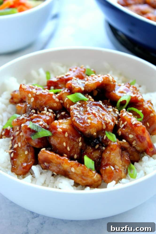Side view of perfectly glazed sesame chicken on white rice, served in a pristine white bowl, ready to be enjoyed.