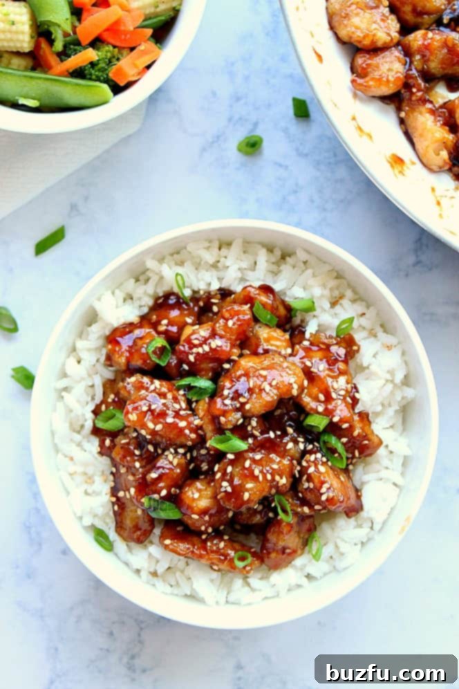 Overhead shot of succulent sesame chicken served over white rice, elegantly garnished with finely chopped green onions, showcasing a delicious meal.