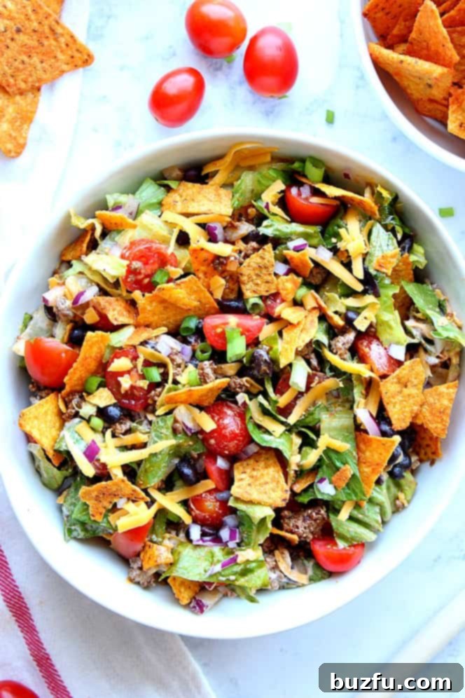 Dorito Taco Salad Recipe - chopped lettuce, tomatoes, seasoned meat, black beans, onions, zesty dressing and crunchy tortilla chips is everything you love about tacos in one tasty salad! Overhead shot of taco salad with tortilla chips, tomatoes, cheese and beans.