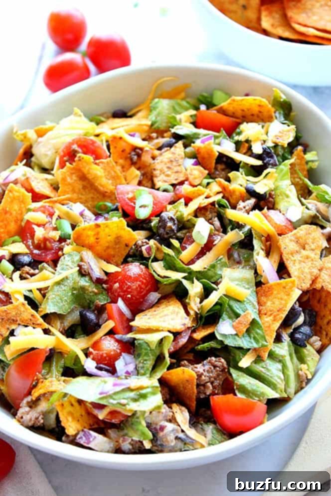 Dorito Taco Salad Recipe - chopped lettuce, tomatoes, seasoned meat, black beans, onions, zesty dressing and crunchy tortilla chips is everything you love about tacos in one tasty salad! Close up shot of Dorito taco salad in white bowl.