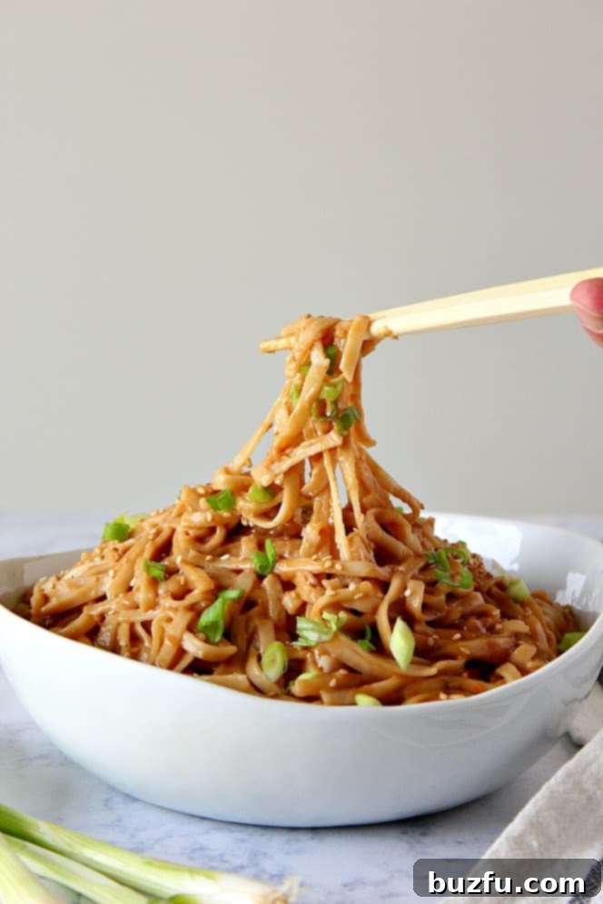 Thai Peanut Noodles Recipe - nutty, slightly spicy sauce tossed with noodles that cooks in just 10 minutes. The easiest and fastest takeout dinner you can make in your own kitchen! Side shot of white bowl filled with peanut noodles lifted by chopsticks.