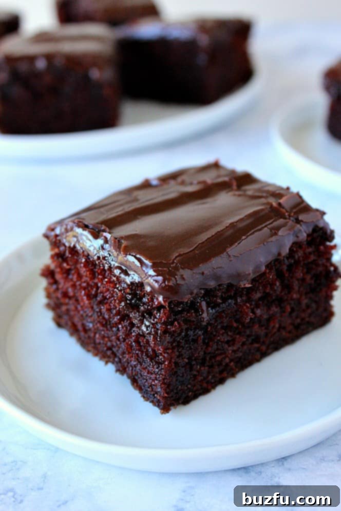 Moist One-Bowl Chocolate Cake with Fudgy Frosting Side shot of a perfect piece of One-Bowl Chocolate Cake with luscious fudgy chocolate frosting, served on a white plate with other plates in background.