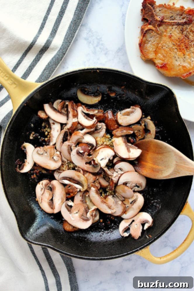 Overhead shot of sliced mushrooms and minced garlic sautéing in melted butter in a hot cast iron skillet.