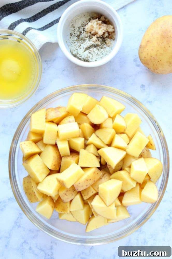 How to make roasted potatoes with ranch and garlic. Overhead shot of freshly chopped potatoes in a clear glass bowl, ready for seasoning.