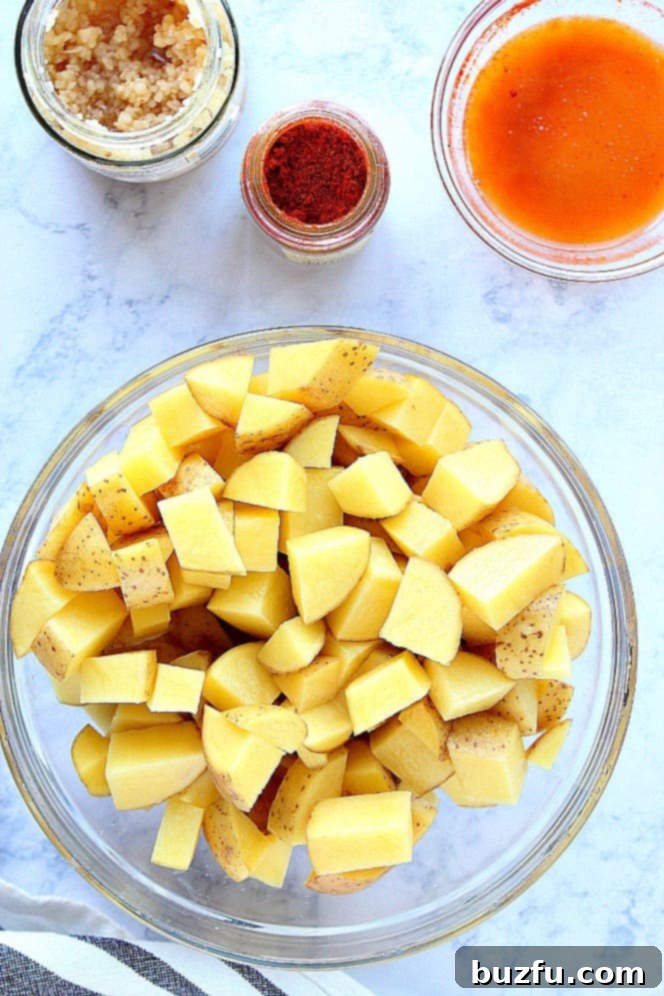 How to make perfect roasted potatoes. Overhead shot of potato chunks in glass bowl, garlic in jar, paprika in jar and melted butter with paprika in a bowl.