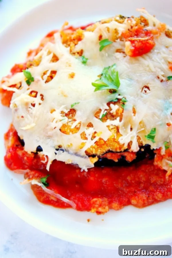 How to make healthier Eggplant Parmesan with half the calories. Cheesy Eggplant Parmesan on a white serving plate.