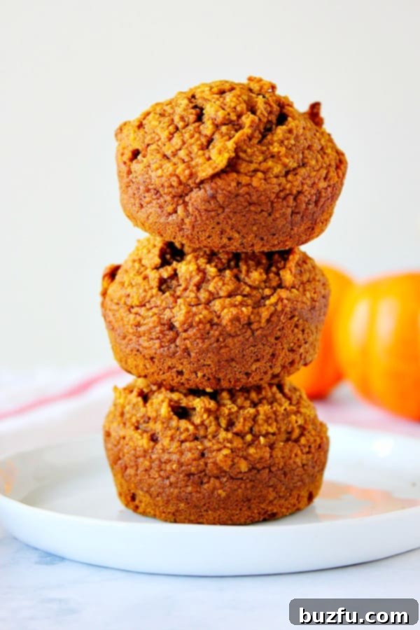 Healthy Pumpkin Muffins Recipe - soft, moist and delicious pumpkin muffins made with oat flour, no dairy or eggs! Each muffin has about 145 calories. Three Healthy Pumpkin Muffins stacked on each other, showcasing their perfectly domed tops and soft texture.