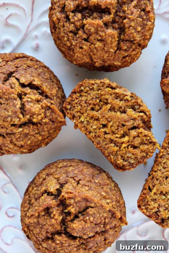 Healthy Pumpkin Muffins - soft, moist and delicious pumpkin muffins made with oat flour, no dairy or eggs! Each muffin has about 145 calories. Overhead shot of healthy pumpkin muffins on a pristine white plate, with one muffin delicately cut through to reveal its moist, soft interior.