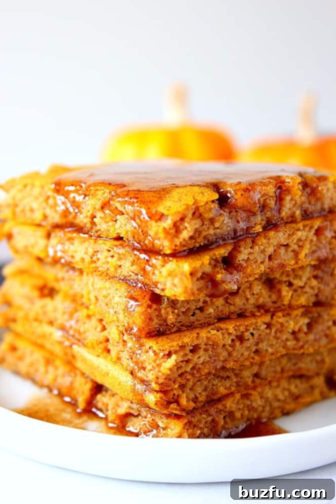 Pumpkin Sheet Pan Pancakes Recipe - soft, fluffy and filled with pumpkin and pumpkin spice pancakes baked in the oven on a sheet pan. No more flipping! Serve with spiced brown sugar butter. Close up shot of pumpkin pancakes stacked on white plate, with a drizzle of melted butter.
