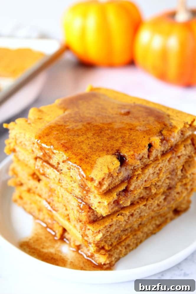 Pumpkin Sheet Pan Pancakes Recipe - soft, fluffy and filled with pumpkin and pumpkin spice pancakes baked in the oven on a sheet pan. No more flipping! Serve with spiced brown sugar butter. Pumpkin sheet pan pancakes stack on white plate, with pumpkins in the background.