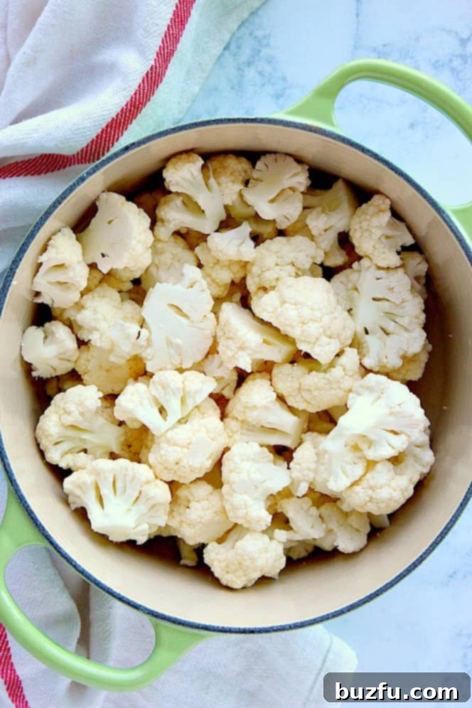 Overhead shot of cauliflower florets in a vibrant green cooking pot.