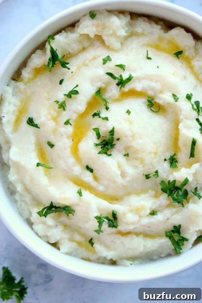Overhead shot of creamy mashed cauliflower in a serving bowl, garnished with chopped parsley.