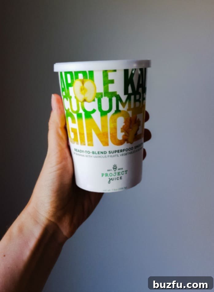 A hand holds up a Sub-Zero Superfoods smoothie cup against a muted wall, highlighting its convenient design.