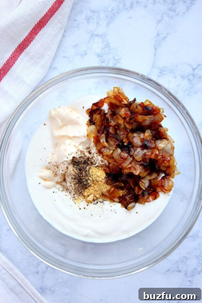 Caramelized Onion Dip Recipe - creamy and flavorful appetizer featuring rich and flavorful caramelized onions. Serve with potato chips for the classic combo or with veggie sticks. Overhead shot of ingredients: caramelized onions, sour cream, mayo, pepper and garlic powder in glass mixing bowl.