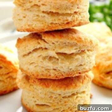 Flaky buttermilk biscuits stacked on white plate.