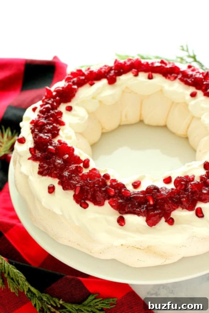 Side shot of Pavlova dessert with cranberry sauce on white cake stand. 