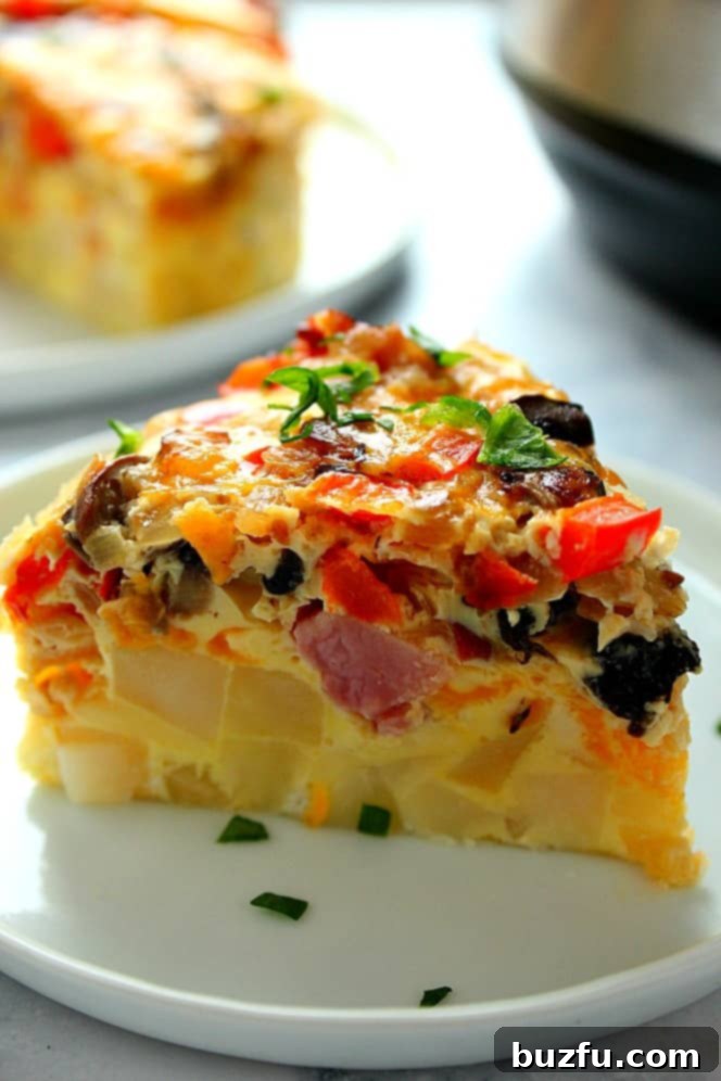 Side shot close up of a slice of breakfast egg casserole with potatoes, ham and veggies, set on white plate.