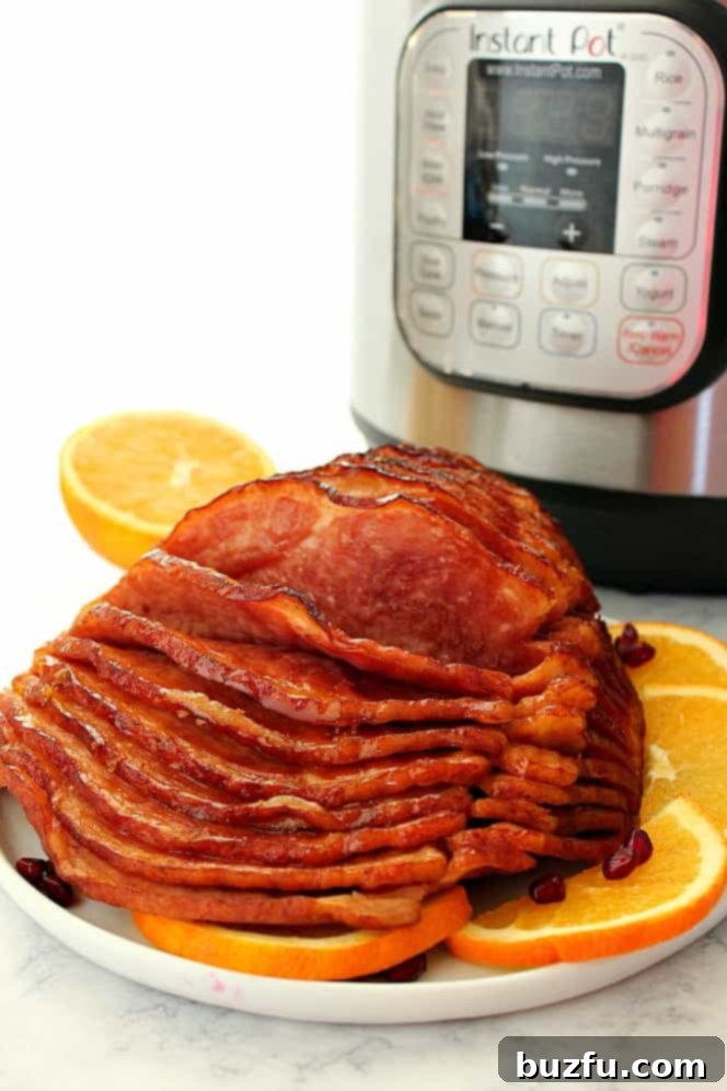 A beautifully cooked spiral-cut ham on a white plate, garnished with fresh orange slices, with an Instant Pot softly blurred in the background, ready to be served.