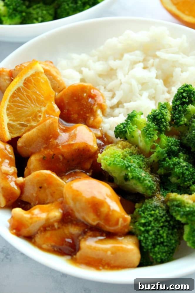 Close up shot of Skinny Orange Chicken with broccoli and rice in a bowl, garnished with green onions.
