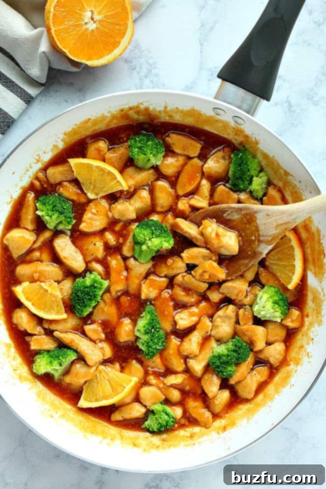 Overhead shot of chicken in bite size pieces in orange sauce in white skillet.