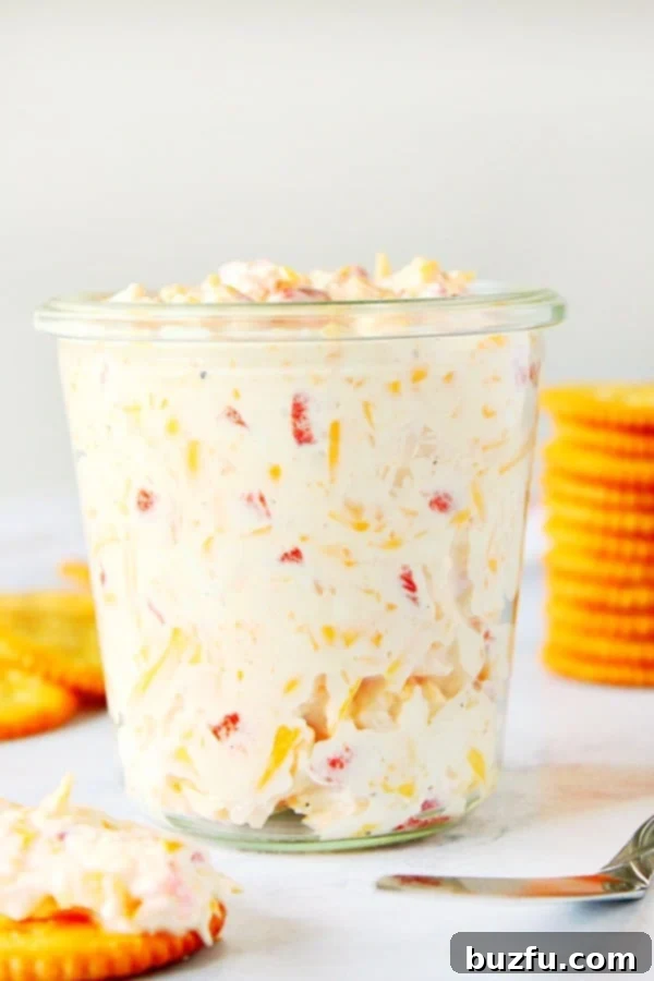 Classic Pimento Cheese Spread, creamy and vibrant, served in an elegant glass jar, accompanied by crispy crackers ready for dipping.