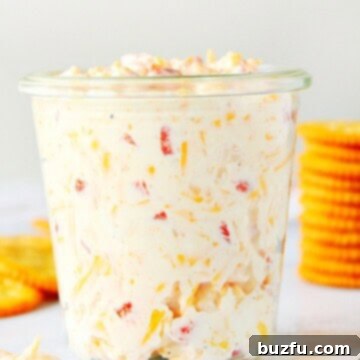 Pimento Cheese Spread in a glass jar, with crackers behind it.