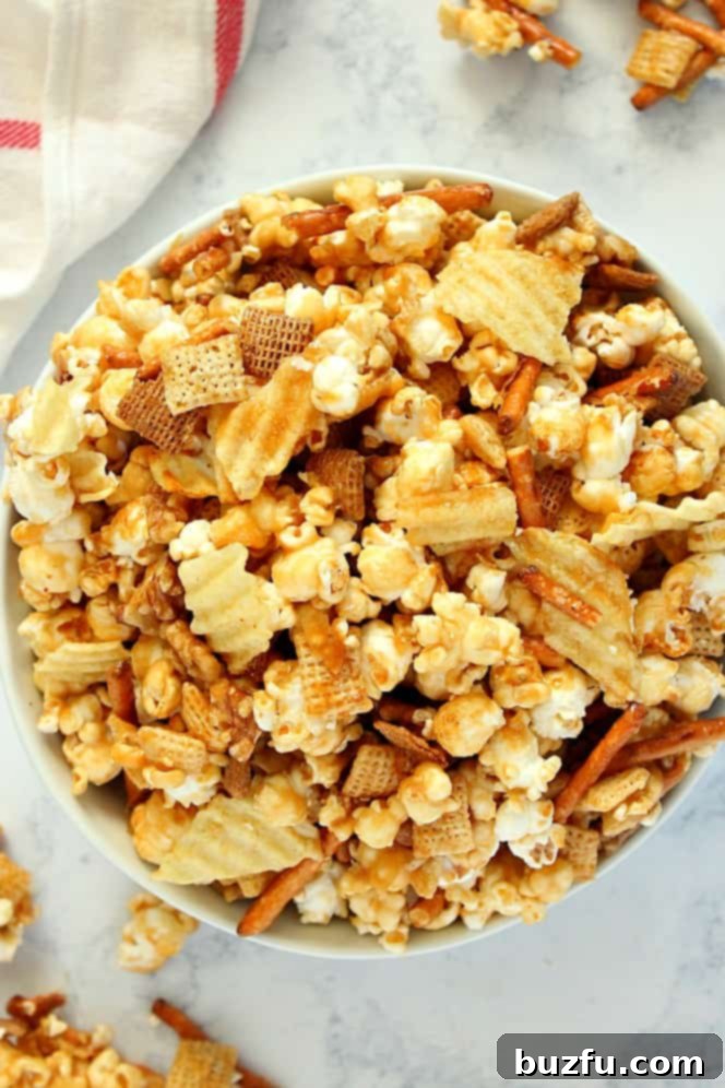 Large white bowl filled with Sweet and Salty Caramel Popcorn Mix, featuring visible pieces of popcorn, pretzels, potato chips, and nuts.