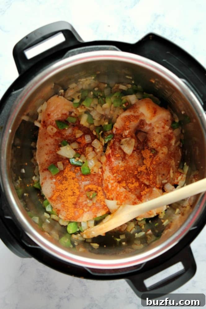 How to make chicken tortilla soup in the Instant Pot. Overhead shot of onions and green peppers sauteed, with two chicken breast in the Instant Pot.