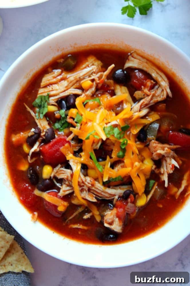 Instant Pot Chicken Tortilla Soup Recipe - healthy and easy soup with black beans, diced tomatoes, corn and chicken. Searing chicken rubbed with spice intensifies the flavor. Overhead shot of white bowl filled with chicken tortilla soup topped with cheddar cheese and cilantro.