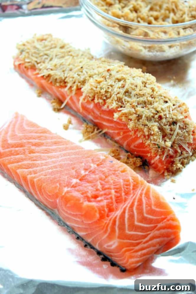 Side shot of two salmon fillets on aluminum foil lined baking sheet, one fillet with breadcrumb Parmesan crust on top.