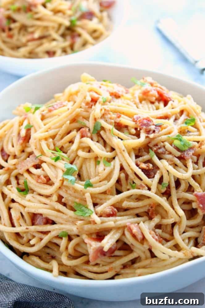 Side shot of spaghetti carbonara with crispy bacon bits and fresh chopped parsley, served in a large white bowl, ready to enjoy.