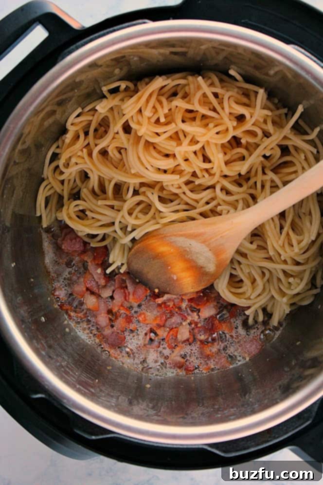 Overhead shot of perfectly cooked spaghetti noodles with crispy bacon in the Instant Pot, ready for the final sauce.
