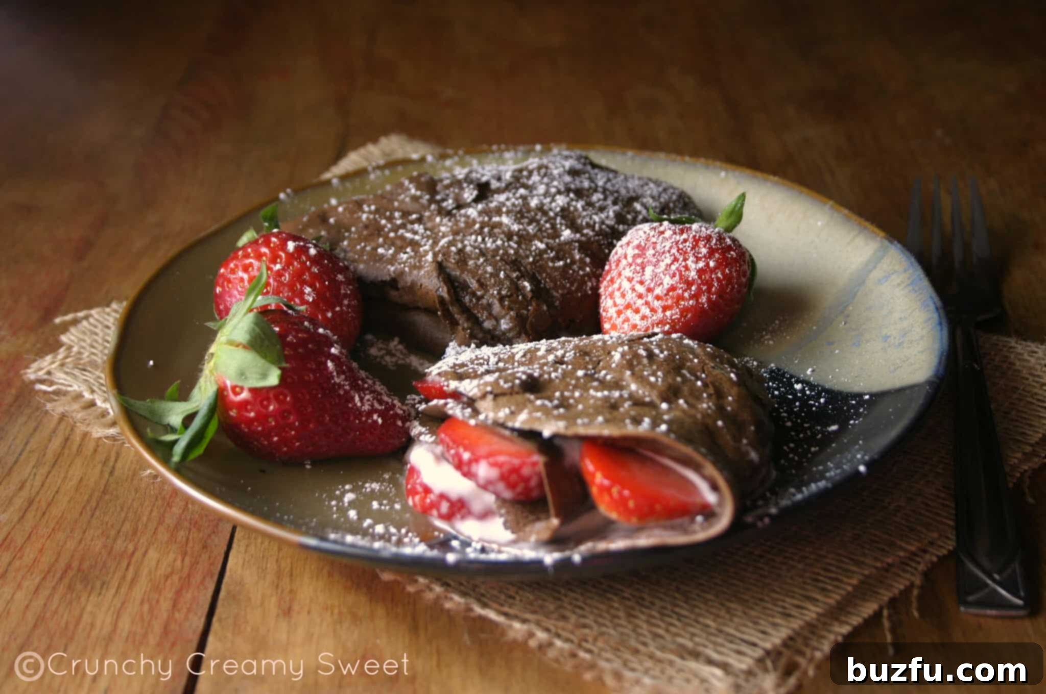 Stacked Chocolate Crepes with Cream Cheese and Strawberries Stack of folded chocolate crepes with cream cheese and strawberries, dusted with powdered sugar, ready for serving.