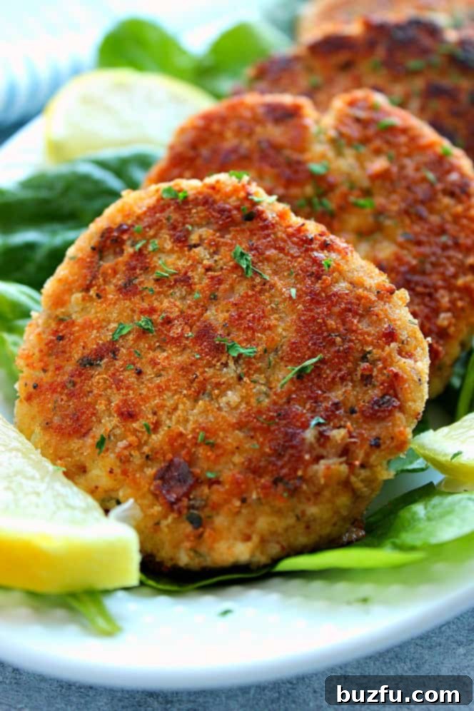 Side close up shot of 4 crispy fried tuna cakes on spinach leaves, with lemon slice on the side. The golden-brown patties are garnished with fresh herbs.