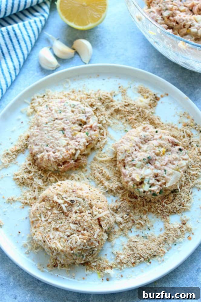 Overhead shot of three raw tuna cakes on a breadcrumb coating in shallow white dish, perfectly shaped and ready for cooking.