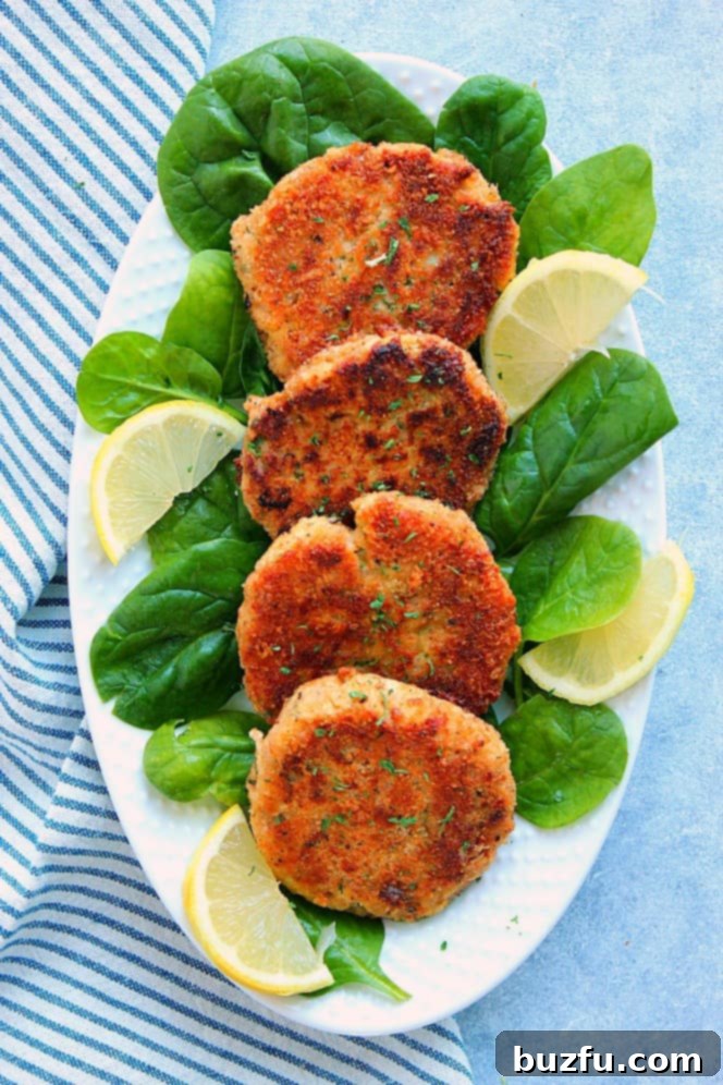 Overhead shot of four tuna cakes on spinach leaves, with lemon slices on the sides, arranged in a white oblong serving dish, ready to be enjoyed.