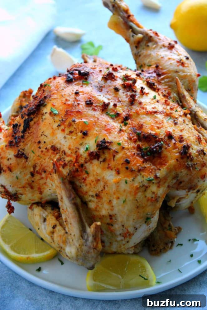 Side shot of roasted chicken with lemon slices on white plate.