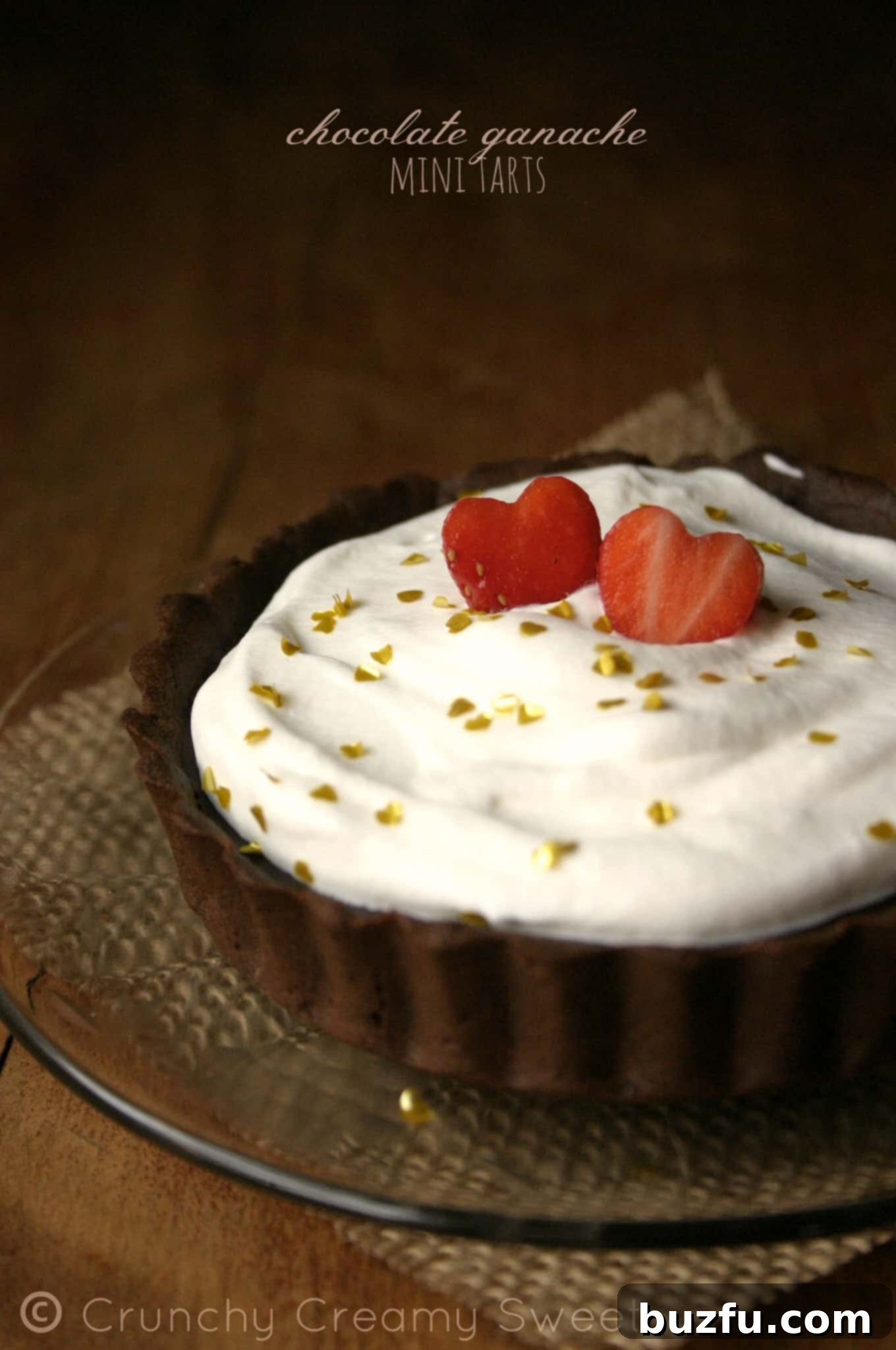 Side shot of a chocolate ganache mini tart with whipped cream topping and a strawberry heart. A beautiful, bite-sized dessert.