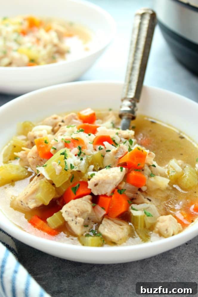 Side shot of chicken and rice soup in a white bowl, with another bowl and Instant Pot in the background, ready to be served.