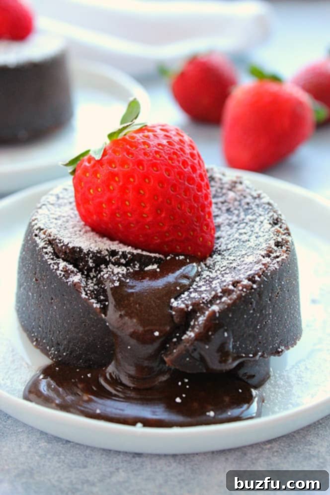 Instant Pot Chocolate Lava Cake Recipe - very easy and decadent molten lava cakes cooked in the Instant Pot pressure cooker, ready in less than 20 minutes. The gooey, fudgy center is irresistible! #InstantPot #chocolate #lavacake #dessert Side shot of chocolate lava cake with gooey center, strawberry on top, set on white plate.