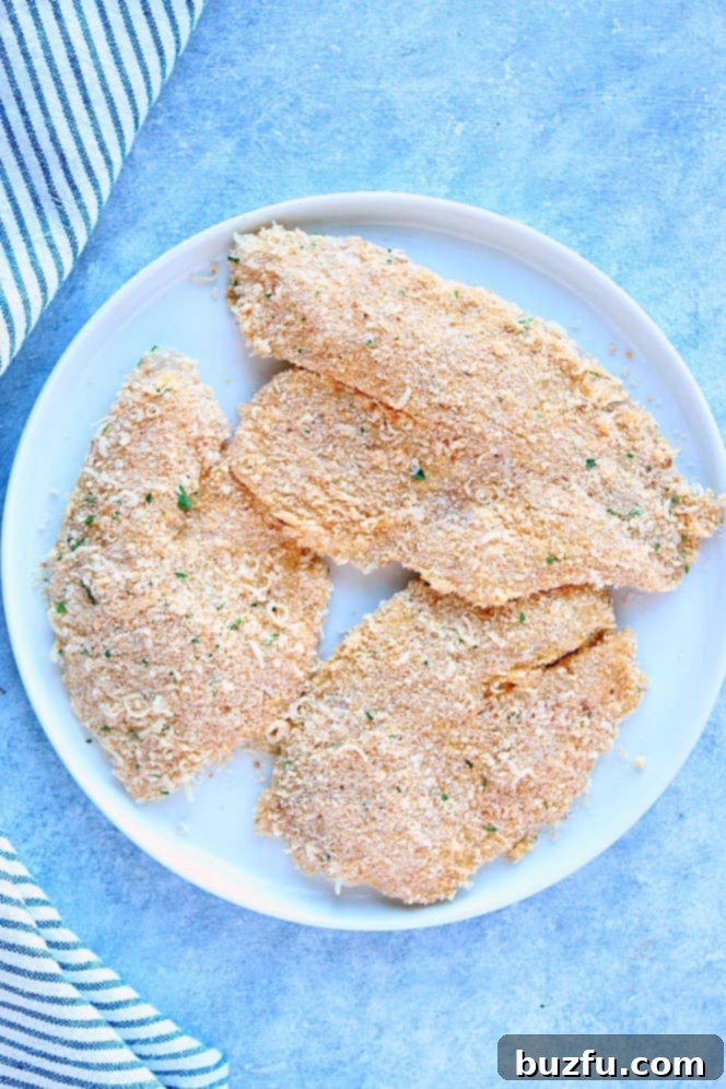 Overhead shot of three tilapia fillets, breaded on white plate.