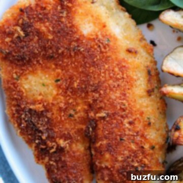 Crispy tilapia on a plate with fries and spinach.